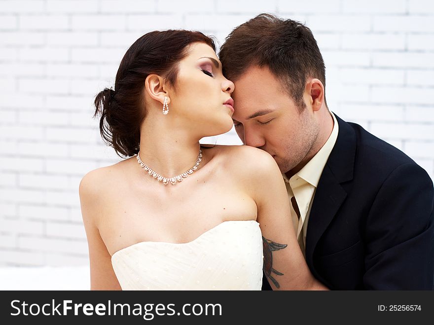 Groom kisses bride in white room