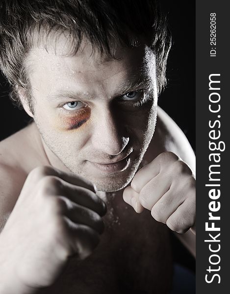 Portrait of a man with a bruise in a battle position. Clenched fists. Dark background. Portrait of a man with a bruise in a battle position. Clenched fists. Dark background.