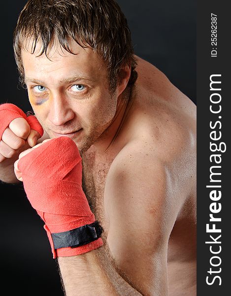 Portrait of a man with a bruise in a battle position. Clenched fists. Dark background. Portrait of a man with a bruise in a battle position. Clenched fists. Dark background.