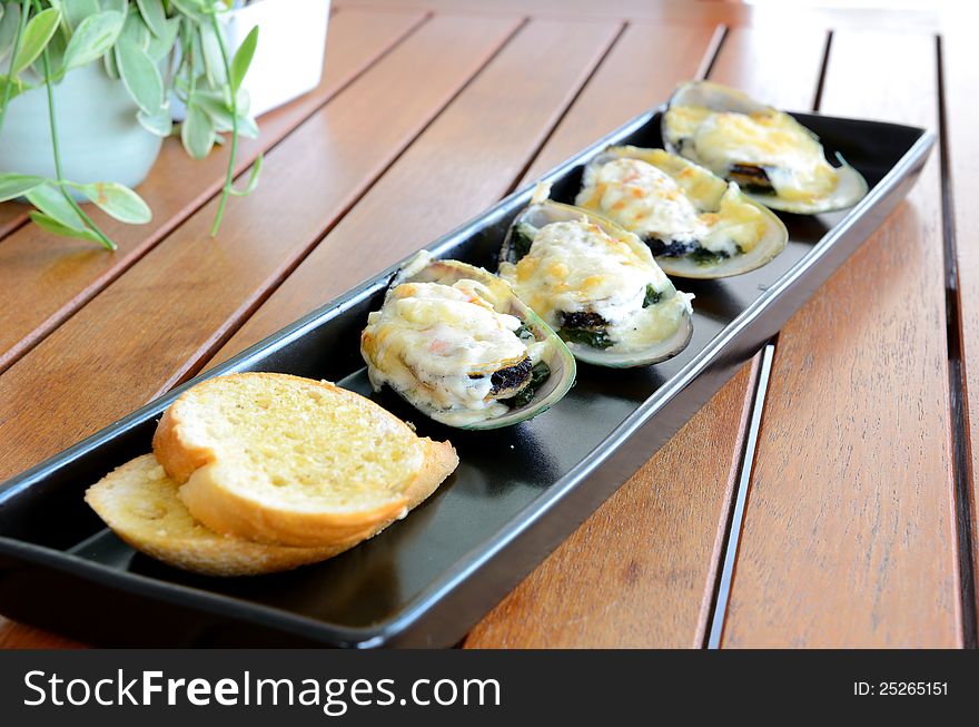 Side view of food call Baked mussel with cheese served on the wooden table.