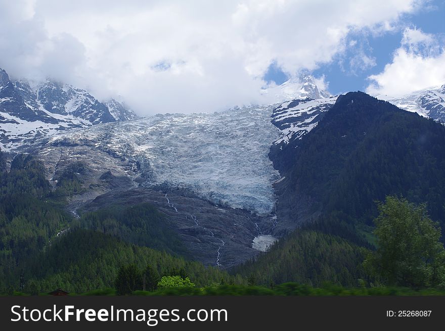Glacier in the Alps with water stream flowed from it down to green trees. Glacier in the Alps with water stream flowed from it down to green trees.