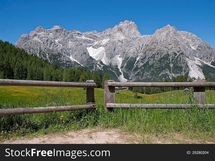 A fence path in italian Alps with glacier in the background and blu sky and green grass field. A fence path in italian Alps with glacier in the background and blu sky and green grass field