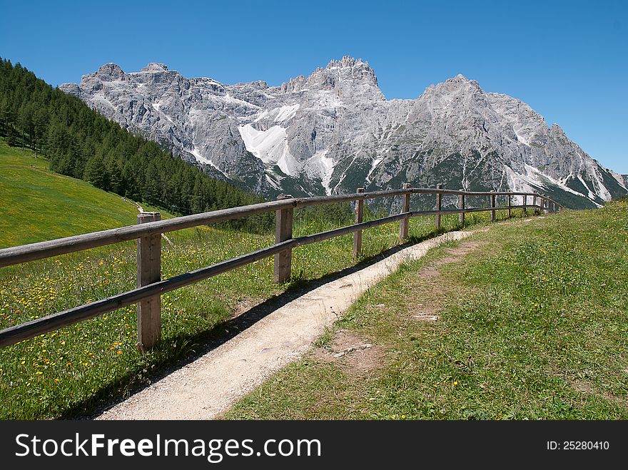 A fence path in italian Alps with glacier in the background and blu sky. A fence path in italian Alps with glacier in the background and blu sky