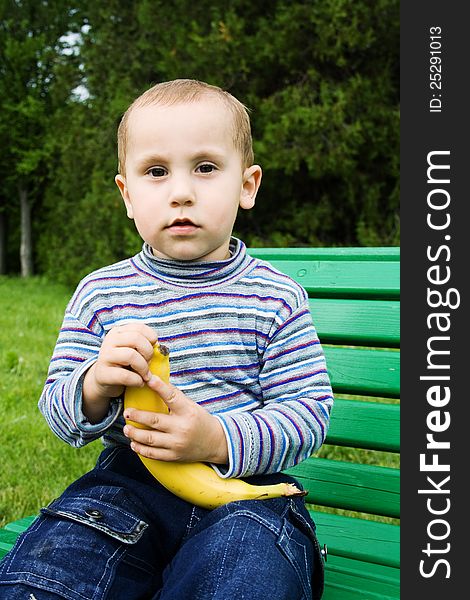 Boy outdoors sitting on a bench and cleans the banana. Boy outdoors sitting on a bench and cleans the banana