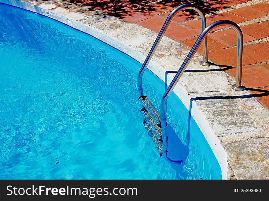 Ladder to swimming pool with blue water.