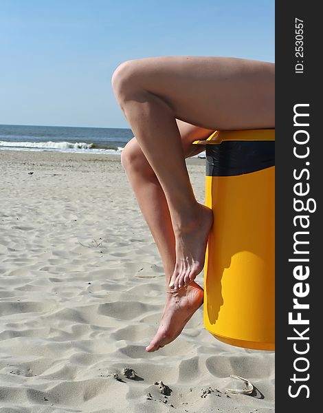 Womans legs on beach waste-bin