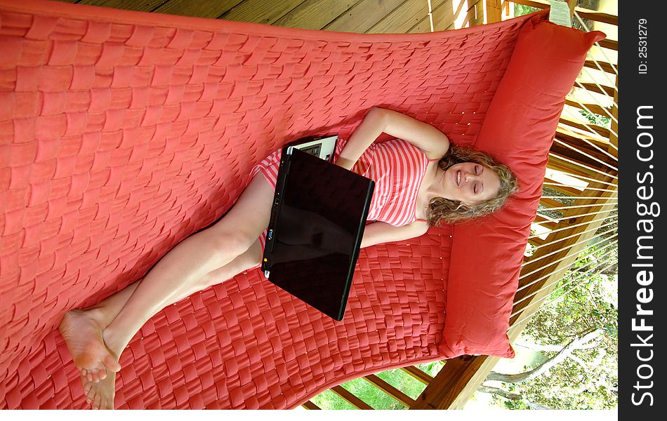 A pretty girl lounging in a hammock on a porch working on her laptop. A pretty girl lounging in a hammock on a porch working on her laptop