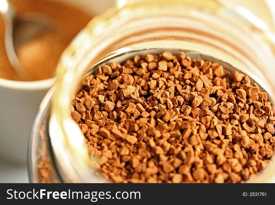 Fresh coffee granules in a jar, with spoon and sugar behind. Fresh coffee granules in a jar, with spoon and sugar behind