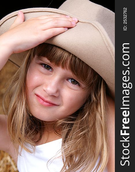 A cute young girl in a cowgirl hat sitting on haybales in a barn