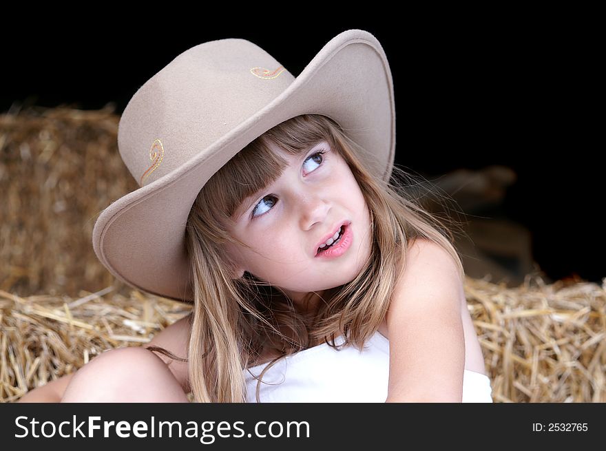 A cute young girl in a cowgirl hat sitting on haybales in a barn. A cute young girl in a cowgirl hat sitting on haybales in a barn