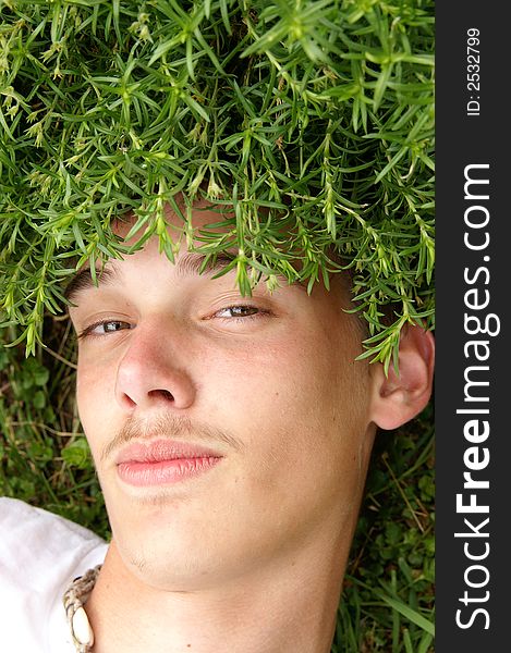 A humorous photo of a teenage boy lying under a green grassy plant. A humorous photo of a teenage boy lying under a green grassy plant