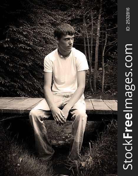 A handsome young man sitting on a bridge, black and white. A handsome young man sitting on a bridge, black and white