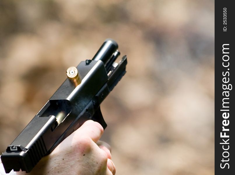 Pistol being fired. The ejected brass is seen halfway between the open chamber and exposed barrel. Also, you can see the next bullet being pushed up from the magazine into the chamber. A small blast of smoke is also present right of the chamber. Pistol being fired. The ejected brass is seen halfway between the open chamber and exposed barrel. Also, you can see the next bullet being pushed up from the magazine into the chamber. A small blast of smoke is also present right of the chamber.