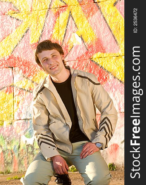 Happy young man sitting next the painted wall. Happy young man sitting next the painted wall