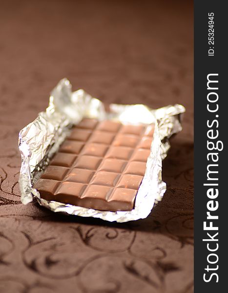 Chocolate bar in tinfoil on brown background