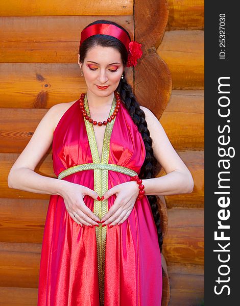 A young girl in a red dress, holding her hand in the shape of a heart on her pregnant belly