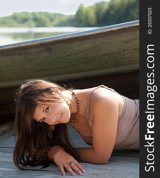 An image gorgeous young woman, smiling sweetly at the viewer, lying on a dock with a boat and lake behind her. An image gorgeous young woman, smiling sweetly at the viewer, lying on a dock with a boat and lake behind her