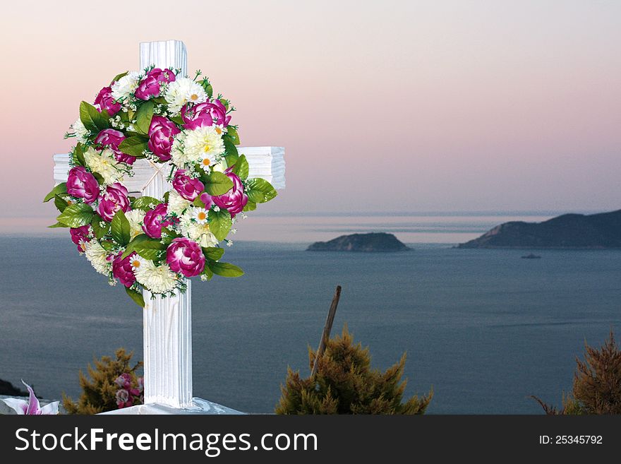 Sea view from cemetery, focus on a wooden white cross with flowers