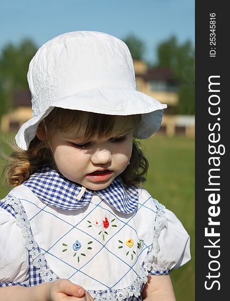 Beautiful little girl wearing dress and white panama looks down outdoor. Beautiful little girl wearing dress and white panama looks down outdoor