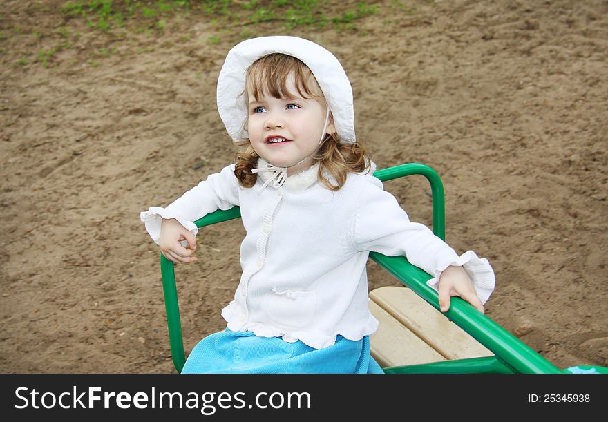 Llittle girl wearing white panama rides on small carousel at playground. Llittle girl wearing white panama rides on small carousel at playground