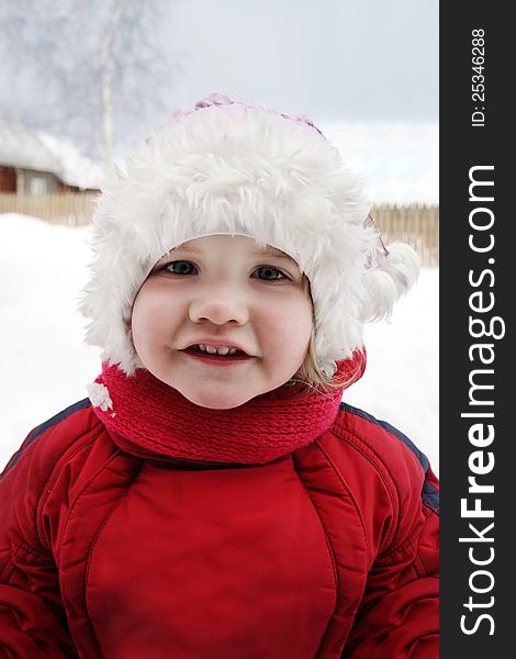 Cute little girl wearing warm clothing stands near home and smiles at winter. Cute little girl wearing warm clothing stands near home and smiles at winter