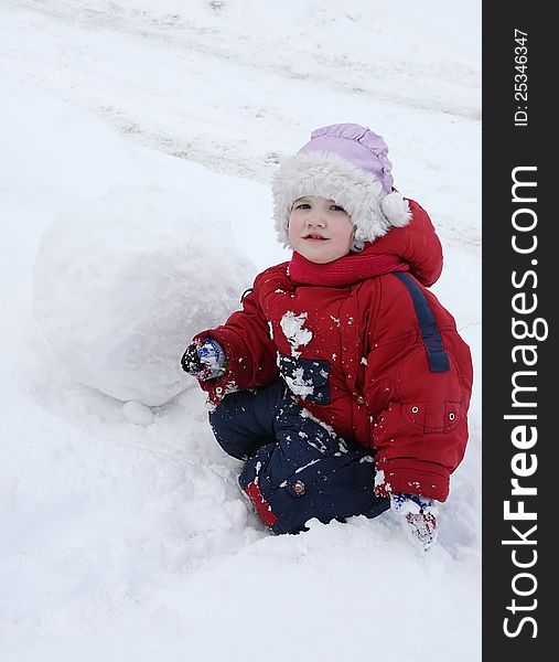 Little tired girl sits on snow near big snowball