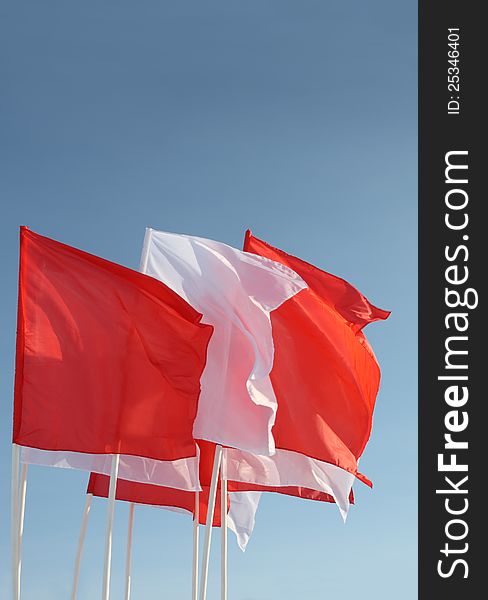 Eight red and white flags flutter in wind on blue sky background