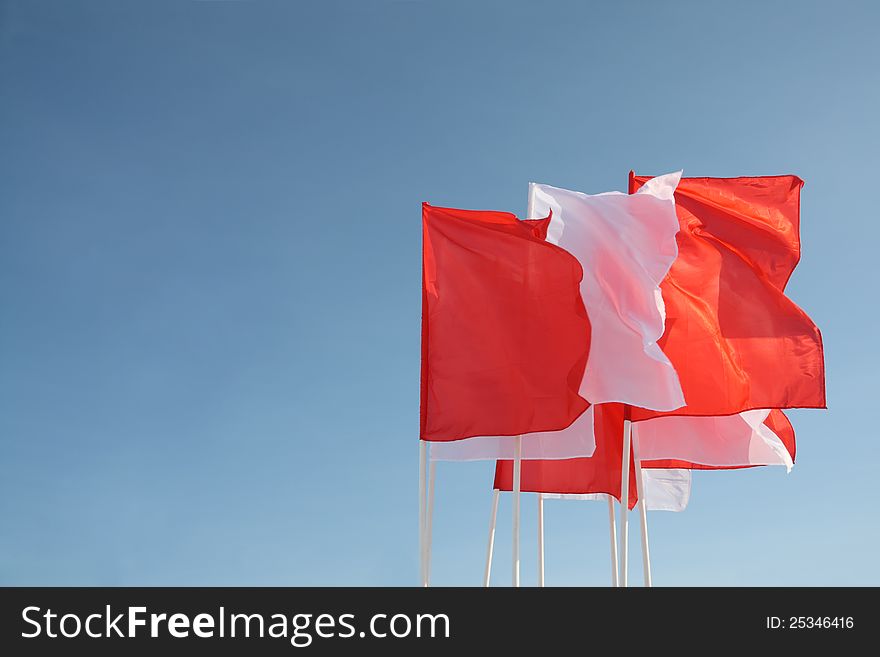 Eight red and white flags flutter in wind at background of blue pure sky