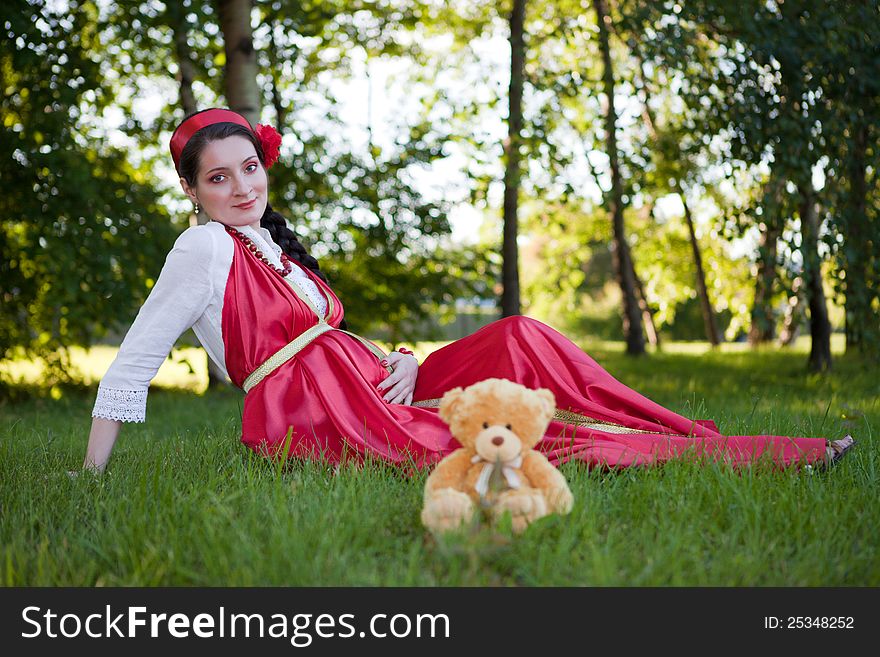 A young pregnant girl sitting on the grass in a red dress
