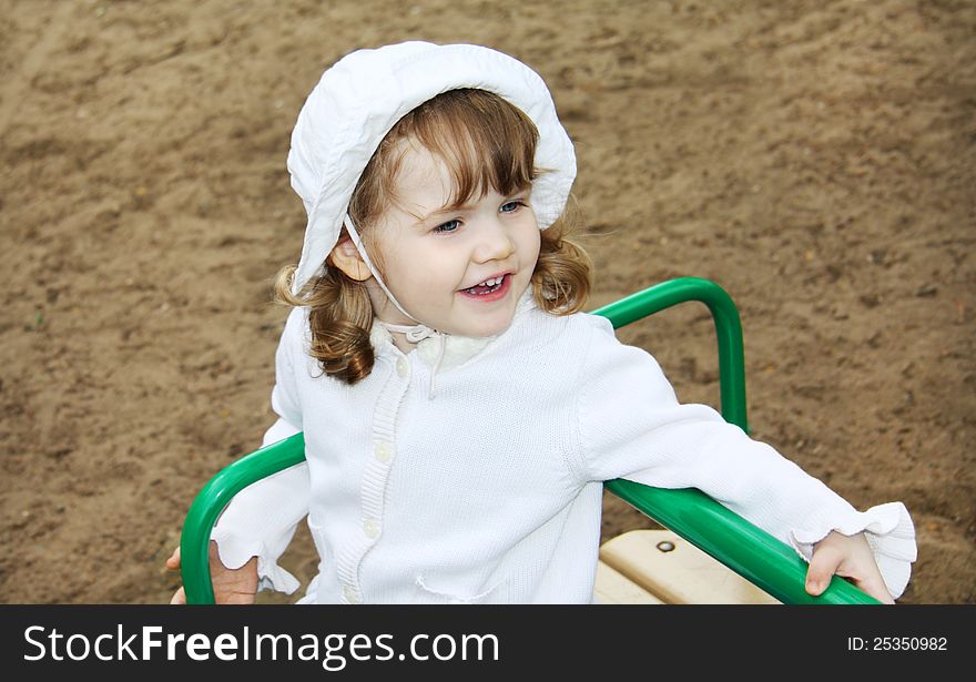 Happy cute girl wearing white panama rides on small carousel at playground. Happy cute girl wearing white panama rides on small carousel at playground