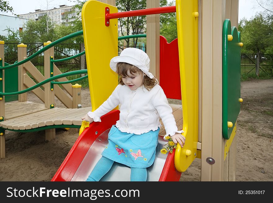 Cute little girl wearing white blouse prepares for rolling at slide in playground. Cute little girl wearing white blouse prepares for rolling at slide in playground