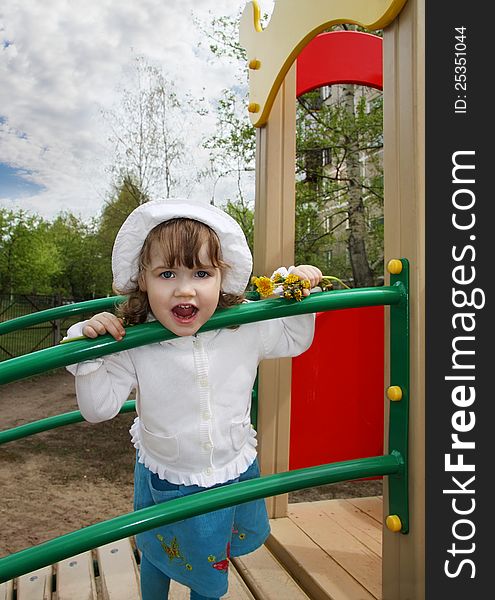 Cute little girl wearing white blouse stands on playground and looks at camera. Cute little girl wearing white blouse stands on playground and looks at camera