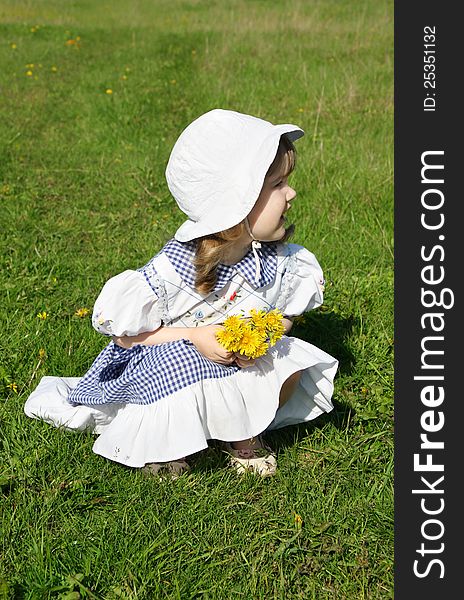 Beautiful little girl wearing dress with yellow dandelions sits on grass and looks into distance. Beautiful little girl wearing dress with yellow dandelions sits on grass and looks into distance