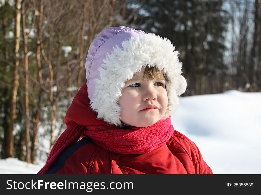 Little sad girl stands in winter forest and looks into distance