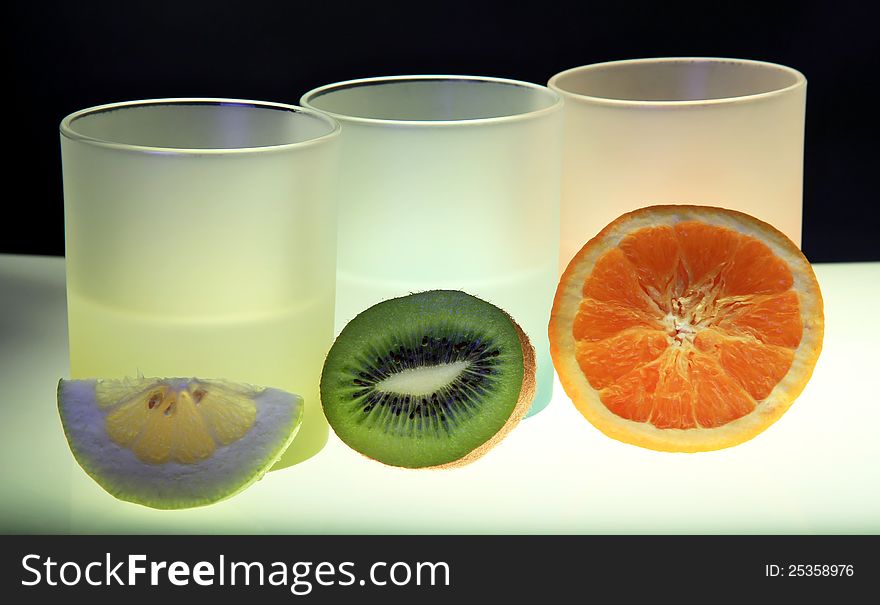 Lighted coloured glasses with kiwi , orange and lemon slices. Black background.