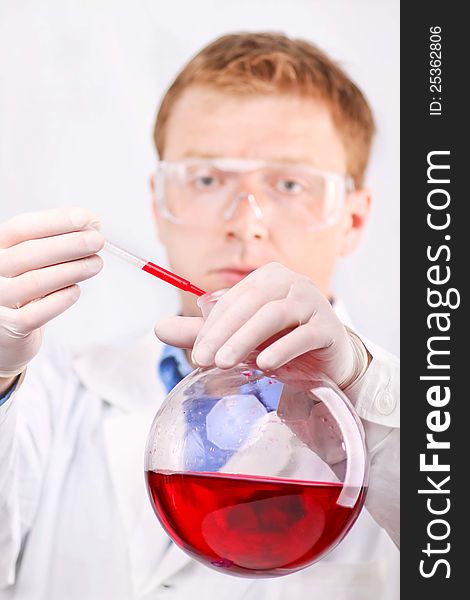 Man in white coat and protective glasses taking red sample from round flask. Man in white coat and protective glasses taking red sample from round flask
