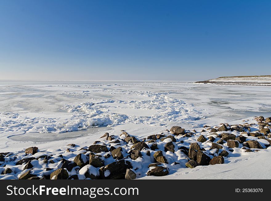 Wide view of a frozen IJsselmeer (lake) in The Netherlands with and protection rocks. Wide view of a frozen IJsselmeer (lake) in The Netherlands with and protection rocks.