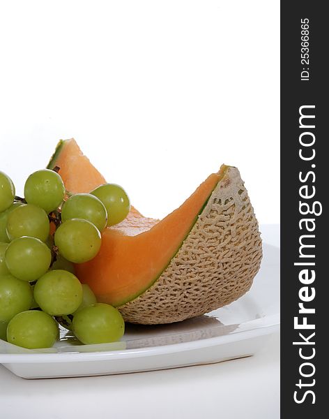 A slice of fresh cantaloupe melon and green grapes on a white plate.  Isolated. A slice of fresh cantaloupe melon and green grapes on a white plate.  Isolated.