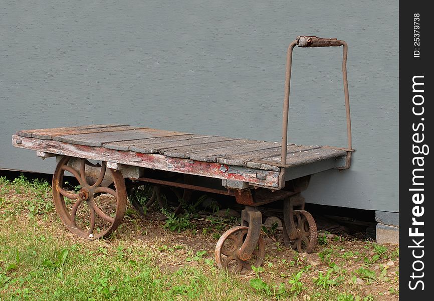 Old wooden and metal push cart used for baggage on a railway station platform, against a gray wall. Old wooden and metal push cart used for baggage on a railway station platform, against a gray wall.
