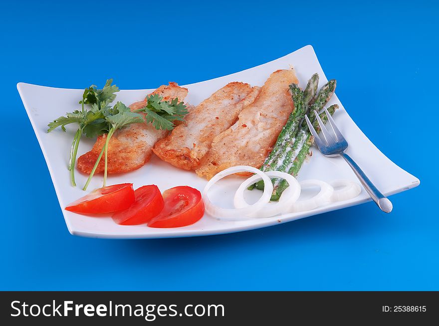 Fish fried in pastry with asparagus and tomatoes against a blue background. Fish fried in pastry with asparagus and tomatoes against a blue background