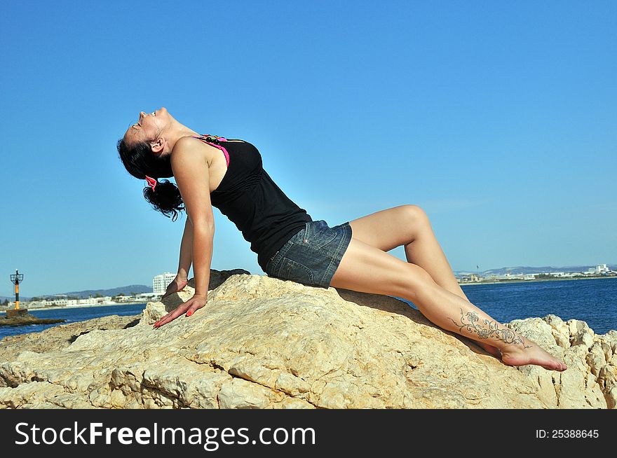 Young girl lying on the rocks on the beach face to the sun. Young girl lying on the rocks on the beach face to the sun