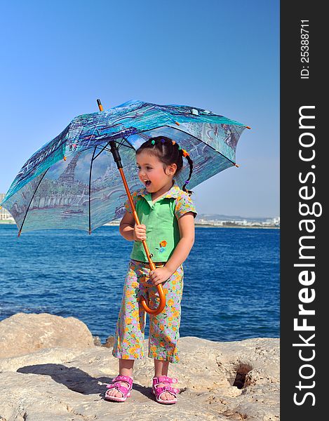 Little girl stands on a rock with an umbrella on the beach and laughing. Little girl stands on a rock with an umbrella on the beach and laughing