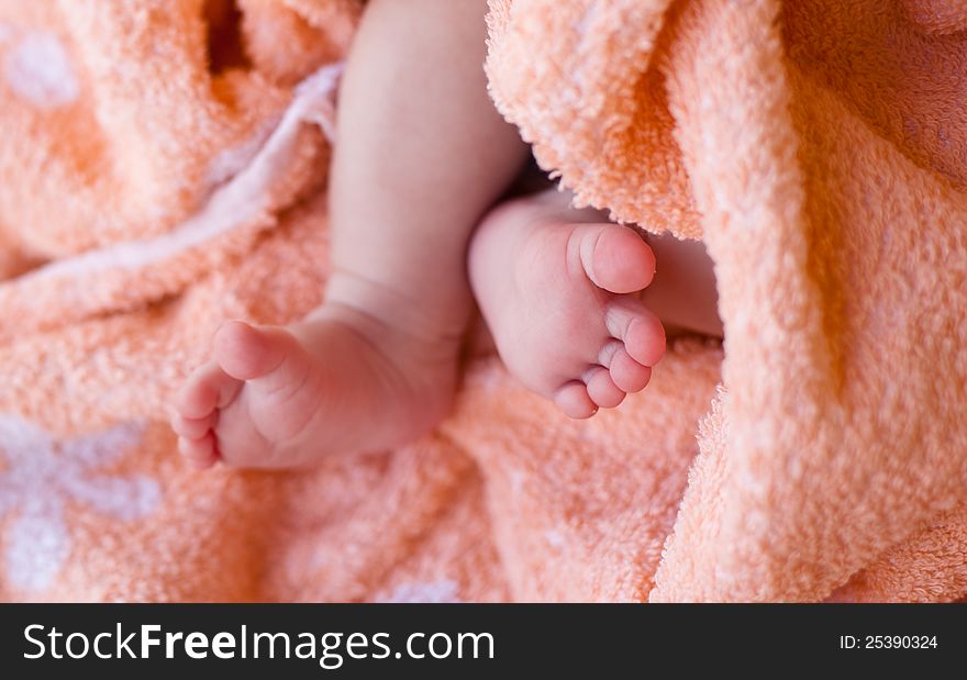 Small baby feet on an orange with white flowers towel. Small baby feet on an orange with white flowers towel
