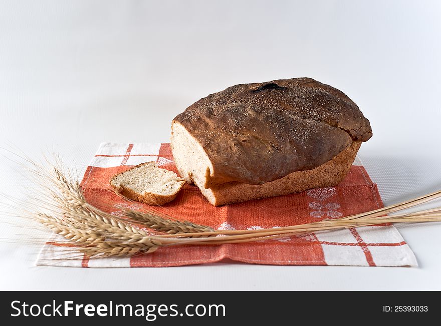 Loaf and slice of white wheat bread with wheatears on the red table-napkin. Loaf and slice of white wheat bread with wheatears on the red table-napkin