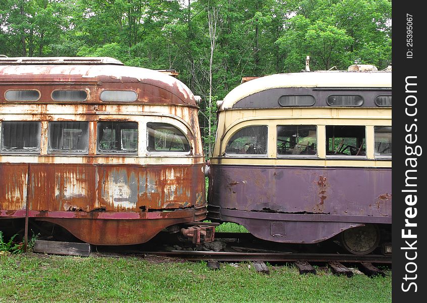 Close-up of the fronts of two old and weathered electric streetcars parked nose to nose in the woods. Close-up of the fronts of two old and weathered electric streetcars parked nose to nose in the woods.
