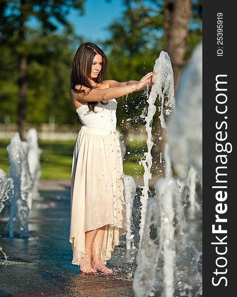 Young beautiful brunette girl playing at outdoor water fountain.Sunny day. Young beautiful brunette girl playing at outdoor water fountain.Sunny day