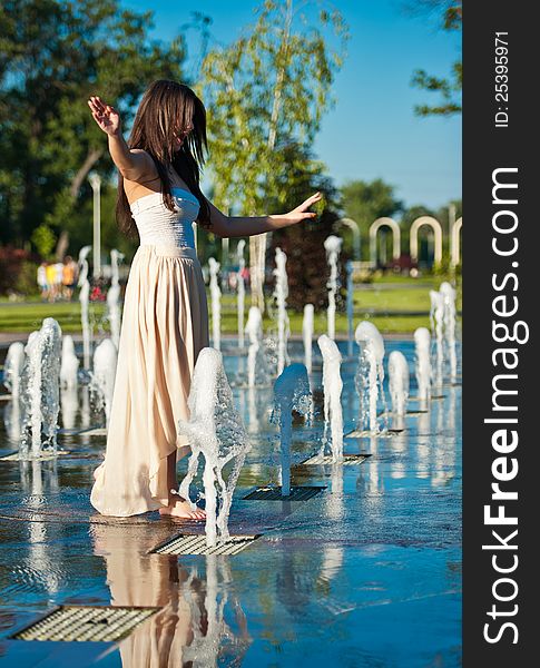 Young beautiful brunette girl playing at outdoor water fountain.Sunny day. Young beautiful brunette girl playing at outdoor water fountain.Sunny day