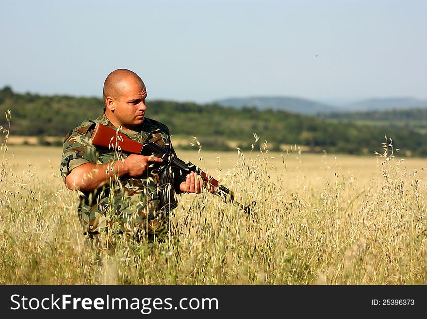 A soldier holding his assault-rifle (ak-47) on a open field.