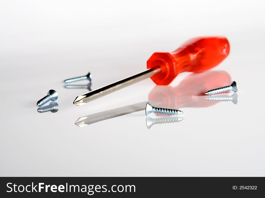 Red screwdriver and four screws on gray background. Red screwdriver and four screws on gray background