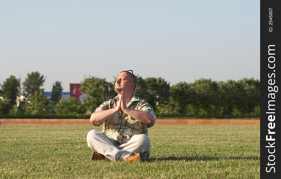 Man in sunglasses meditates sitting on a green grass. Man in sunglasses meditates sitting on a green grass